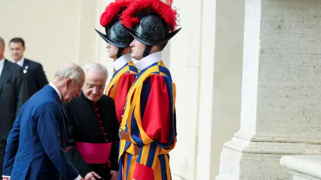 King Charles and Monsignor Leonardo Sapienza walk up the steps. Members of the Swiss Guard can also be seen