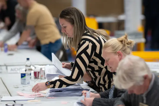 A woman in a black and white top counting papers