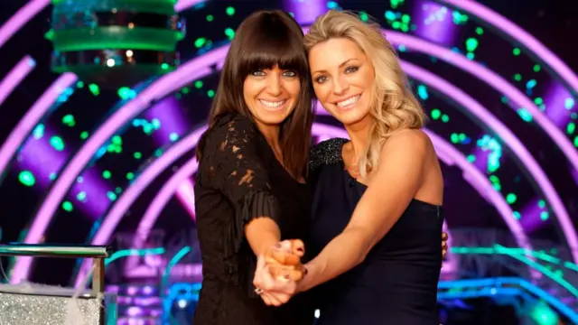 Claudia and Tess hold hands in a Tango style position and smile to camera