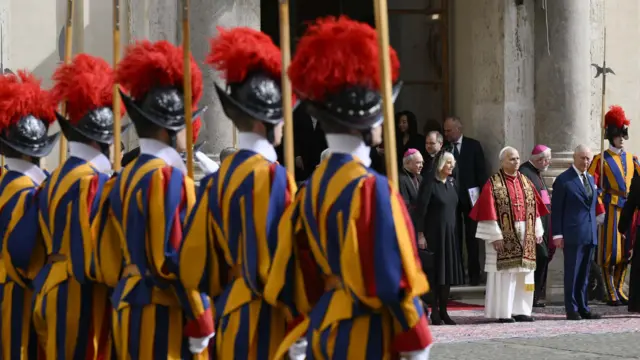 Men in yellow striped outfits and red plumed hats stand to attention