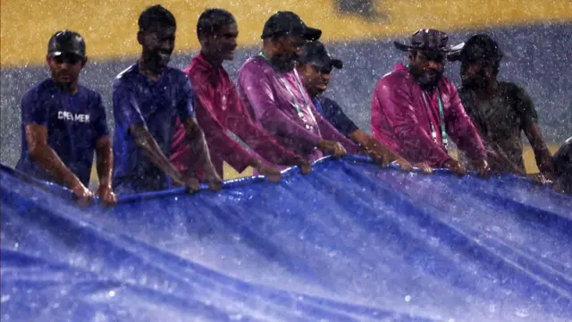 Ground staff bring out the covers as rain interrupts play