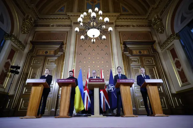 In an ornate room there are five podiums with the five leaders standing behind them. Each podium reads: "Securing our future", and there are flags standing behind them.