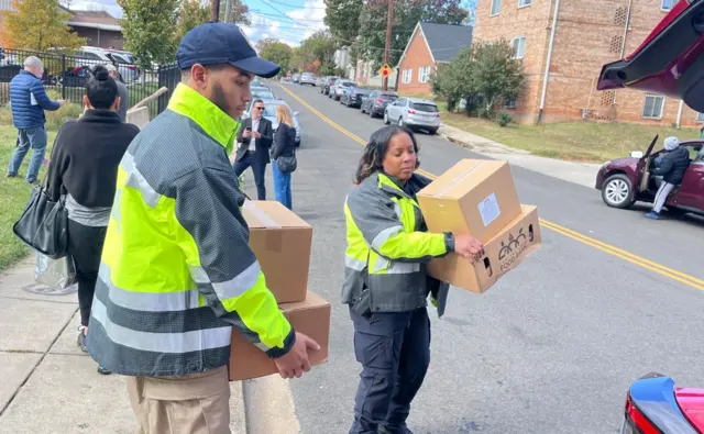 DC officers carrying boxes help load into a car