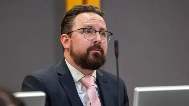 A man with dark hair and beard and glasses