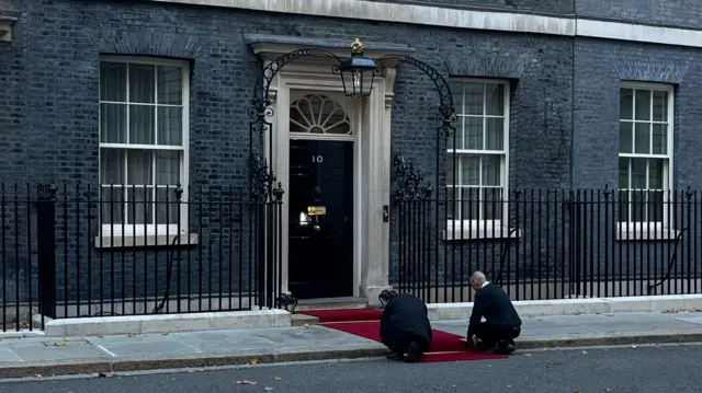 Red carpet being rolled out by two men in front of No 10 Downing Street
