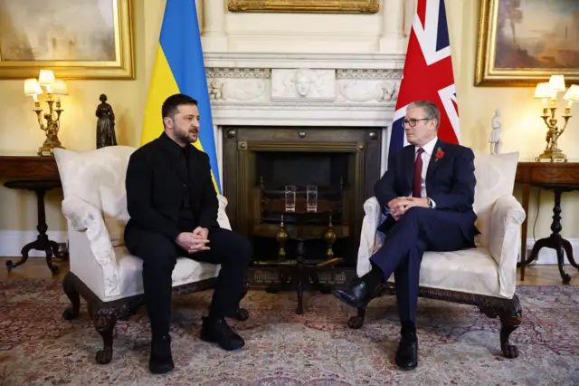 Starmer and Zelensky sit in chairs in front of fireplace, angled slightly towards one another
