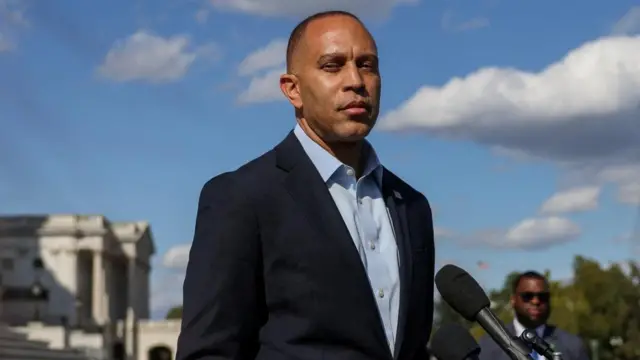 House Minority Leader Hakeem Jeffries, wearing a dark suit and light blue shirt, stand in front of microphones on the steps of the US Capitol