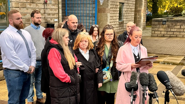 A group of men and women standing outside a court building in front of several microphones.