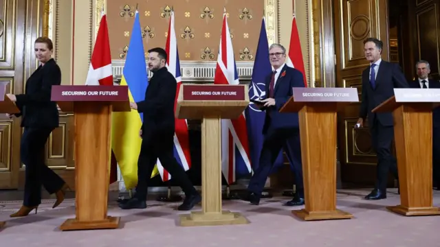 Mette Frederiksen, Volodymyr Zelensky, Keir Starmer, Mark Rutte and Dick Schoof enter a conference room behind podiums and in front of flags