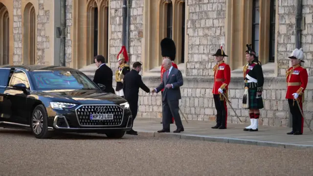 Zelensky (L) clad in black shakes hands with King Charles (R) in a dark grey suit as he steps out of a black car in the Windsor Castle's quadrant