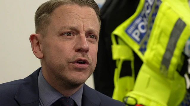 Det Ch Insp Attwell in a dark blue suit with a high-vis jacket in the background