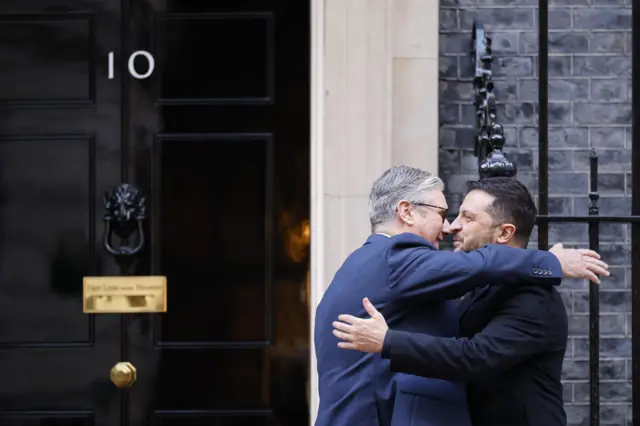 Zelensky and Starmer, both wearing formal clothes, hug while outside the door to No 10 Downing Street