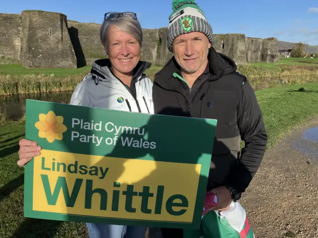 A man and woman stand outside of Caerphilly castle in the sunshine