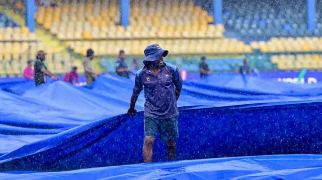 A ground staff covers the pitch as rain delays the start