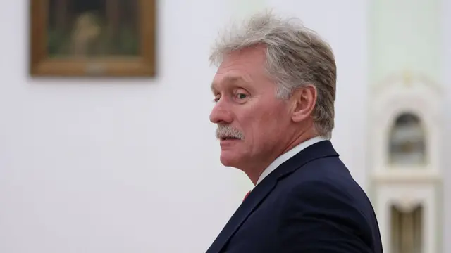 Kremlin spokesman Dmitry Peskov looking to his left as he pictured from the left side, a white wall with a painting in the background