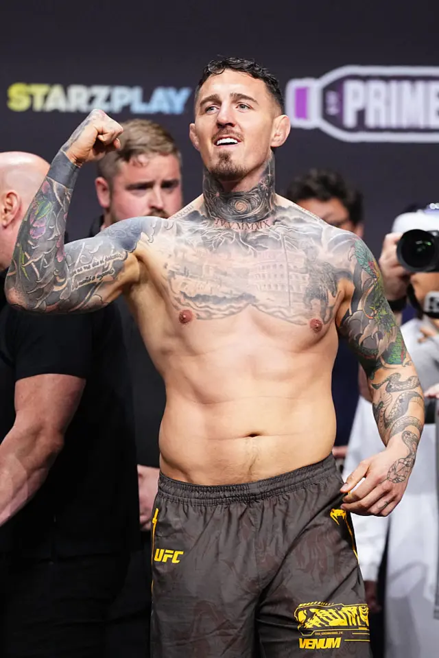 Tom Aspinall holds up his arms as he weighs in for a UFC heavyweight title fight