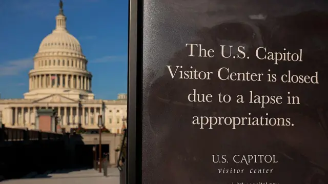 The Capitol in the background with a black sign saying the US Capitol Visitors Center is closed to due to a lapse in appropriations in the foreground.