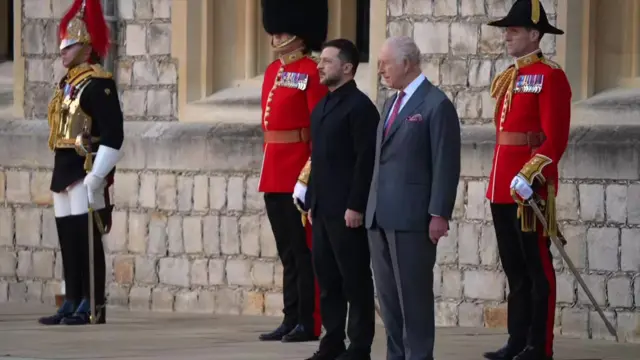 Zelensky (L) and King Charles (R) standing in front of three guardsmen inside the main quadrant of the castle