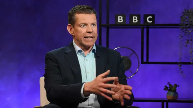 Rhun ap iorwerth pictured sat down infront of a BBC sign to his right taking part in a panorama interview.