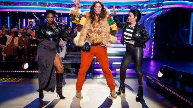 Craig Revel Horwood strikes a pose dressed as a Beatles-era John Lennon, next to Motsi Mabuse as Grace Jones and Shirley Ballas as Elvis