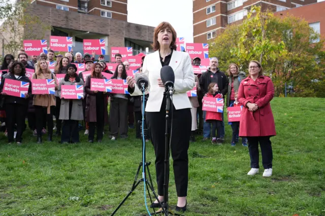 Lucy Powell on a patch of grass with supporters standing behind her