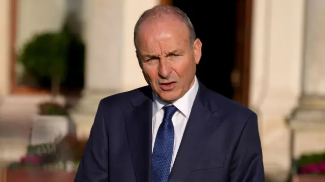 Michéal Martin, with short grey hair, wearing a white shirt, dark blue tie and navy suit
