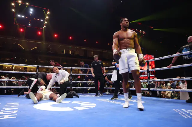 Anthony Joshua walking in the ring with Francis Ngannou flat on his back