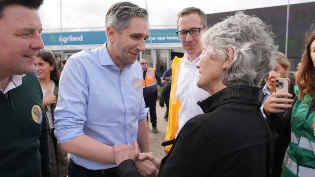 Simon Harris, wearing a blue shirt, shaking hands with Catherine Connolly, wearing a black jacket