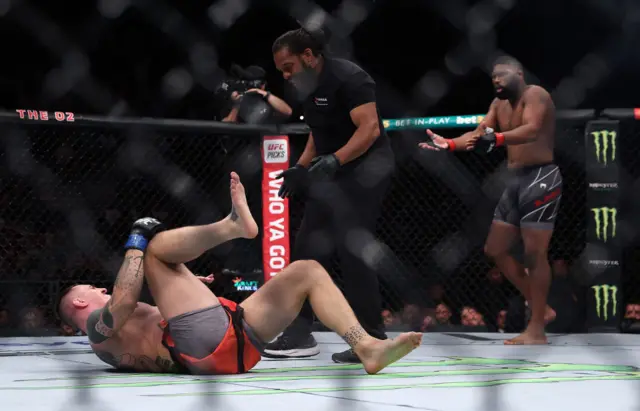 Tom Aspinall lies on his back and holds his knee after suffering an injur