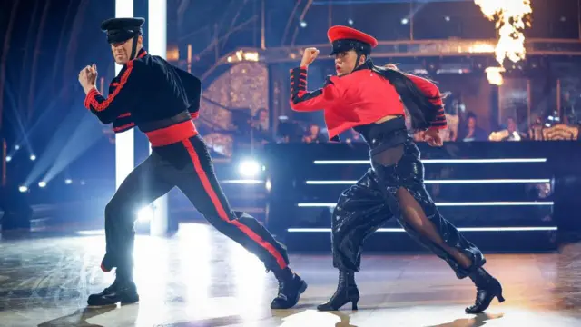 Vicky and her partner, wearing red and black military-style dance outfits, hold a running pose
