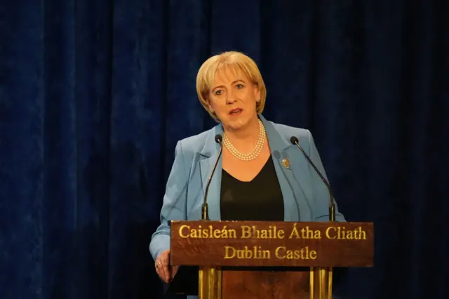 Humphreys is wearing a light blue jacket and a black top with pearls around her neck.