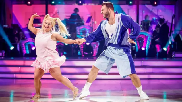 Ellie, who has blonde pigtails, wears a short pink dress and bejewelled gold ballroom shoes