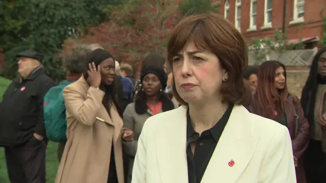 Lucy Powell in front of camera answering questions with crowd of women behind her