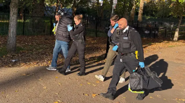 Two female Met Police officers hold onto Hadush Kebatu as he's escorted out of Finsbury Park following his rearrest. Walking alongside them, to the left are two male officers