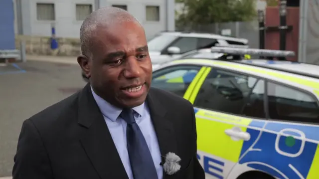 David Lammy speaks while standing in front of a police car