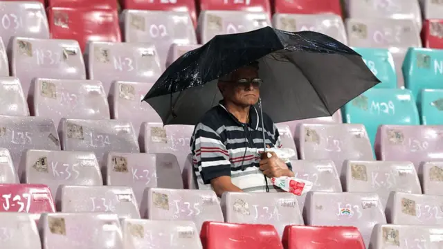 A fan in the stands sits under an umbrella after rain stopped play