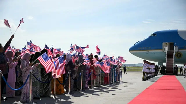 People wave US flags as they wait for US President Donald Trump to walk from Air Force One
