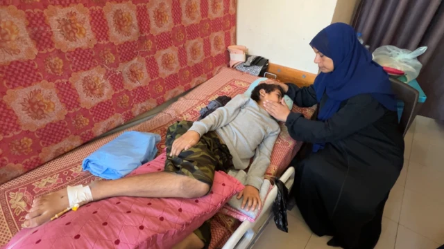 Amar Abu Said, a Palestinian boy, lies on a bed, looking poorly, as a woman touches his face