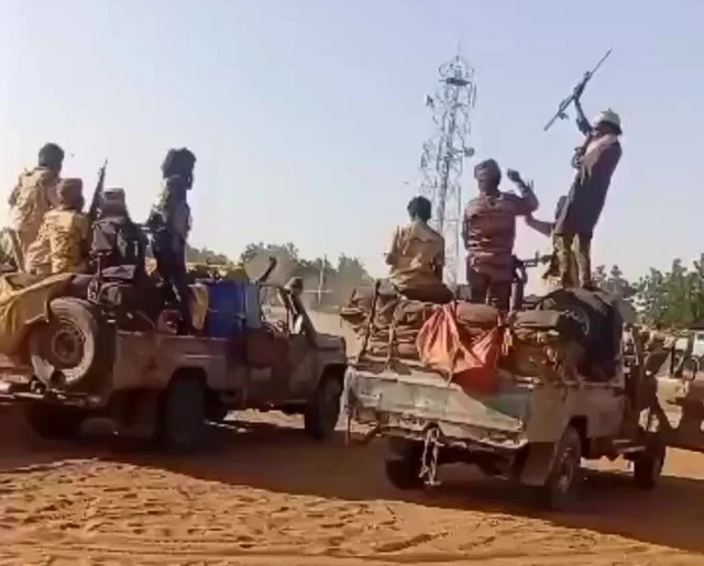Screengrab of a video half a dozen armed RSF fighters sitting or standing on trucks celebrating, a telephone pylon is visible in the background