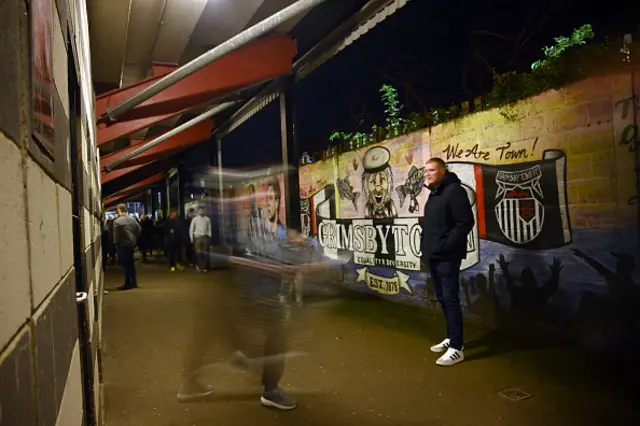 Fans of Grimsby Town walk past a wall outside the stadium