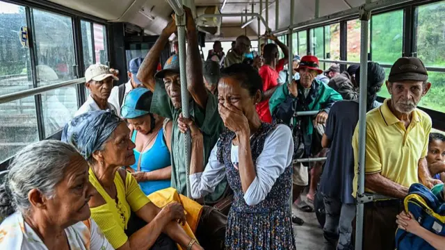 Evacuees on a bus. A woman hold her hand to her mouth and appears to be crying.