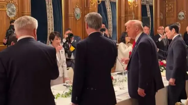 Trump standing opposite Takaichi at a long table, surrounded by aides in suits