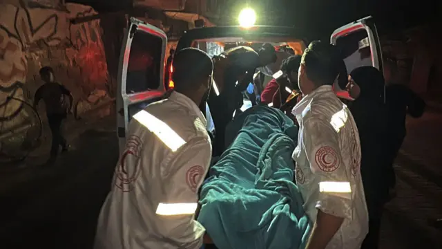 Emergency service workers carry a body covered in a blue blanket