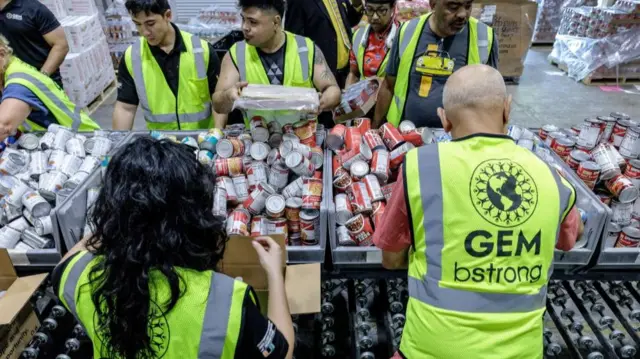Workers in neon vests stand near bins of water and canned food