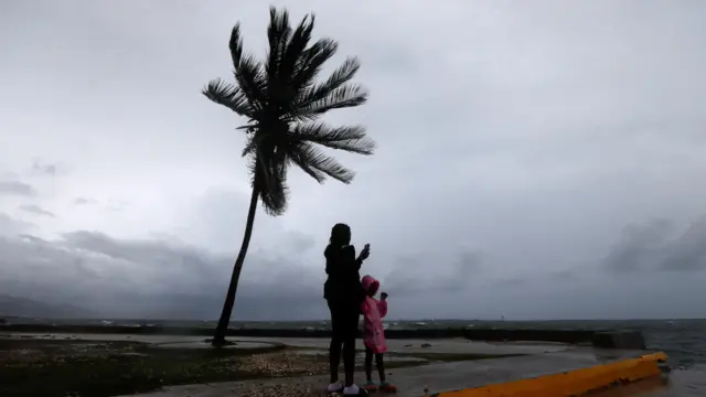 A woman and a child stand along the Kingston waterfront as Hurricane Melissa approaches