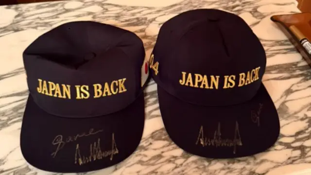 Two black caps signed with gold markers, with bold gold embroidery that reads: Japan is back