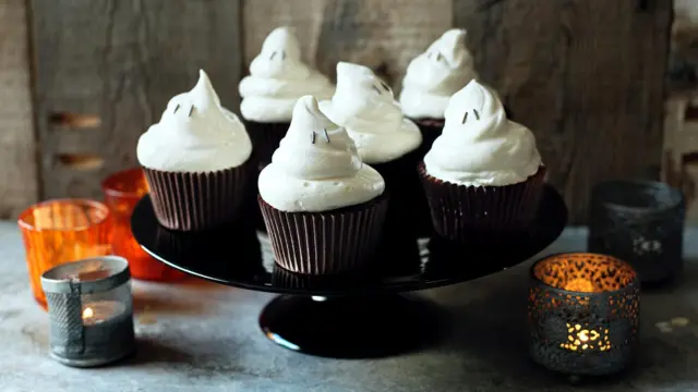 chocolate cupcakes with ghost-shaped icing on top sitting on a serving tray