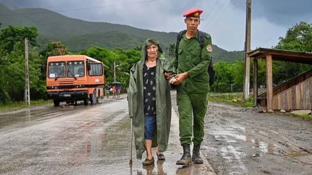 A soldier escorts an older woman down the road