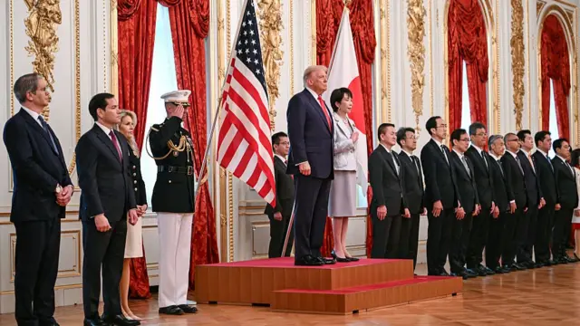 Trump và Takaichi đứng trên bục phát biểu, Takaichi ấn tay trái lên ngực