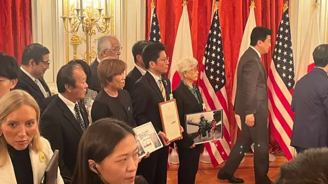 A group of people, dressed in black suites, stand in the room holding framed photos